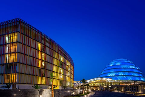 Modern illuminated buildings at night against a blue sky, featuring a curved structure with horizontal lines and a dome-shaped building with blue lighting