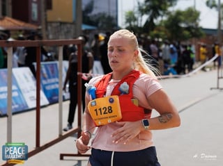 Female runner wearing race bib 1128 jogging through outdoor marathon event with spectators in background