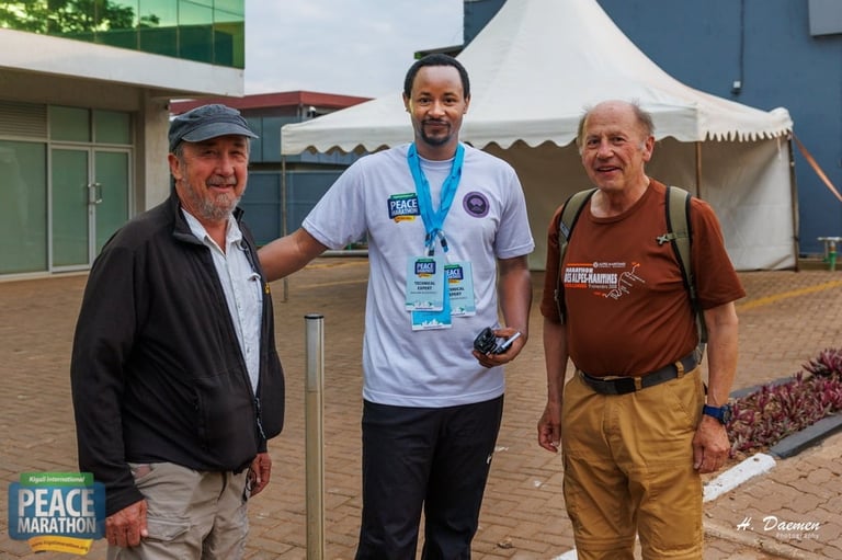 Three men standing together at an outdoor event with tents and buildings in the background at a peace marathon