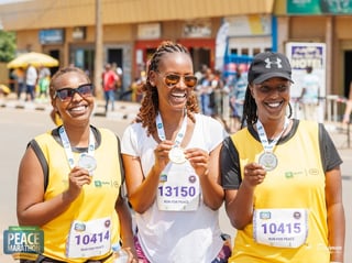 Three smiling women wearing race bibs at a marathon event in a crowded outdoor setting