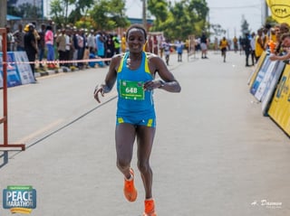 Female marathon runner wearing bib number 648 approaching finish line on city street with spectators and barriers