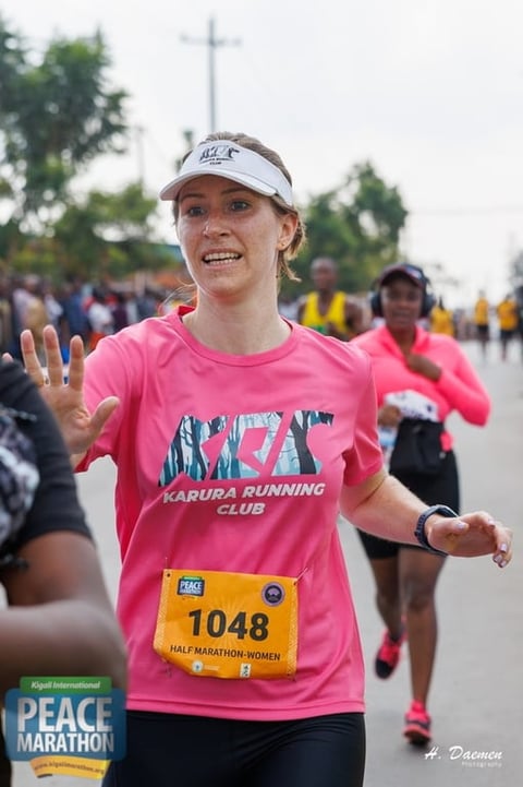 Female marathon runner in pink Karura Running Club shirt with race bib 1048 smiling during Peace Marathon event