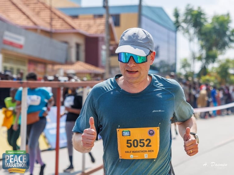 Male runner with race bib 5052 wearing blue shirt, white cap, and sunglasses giving thumbs up during marathon