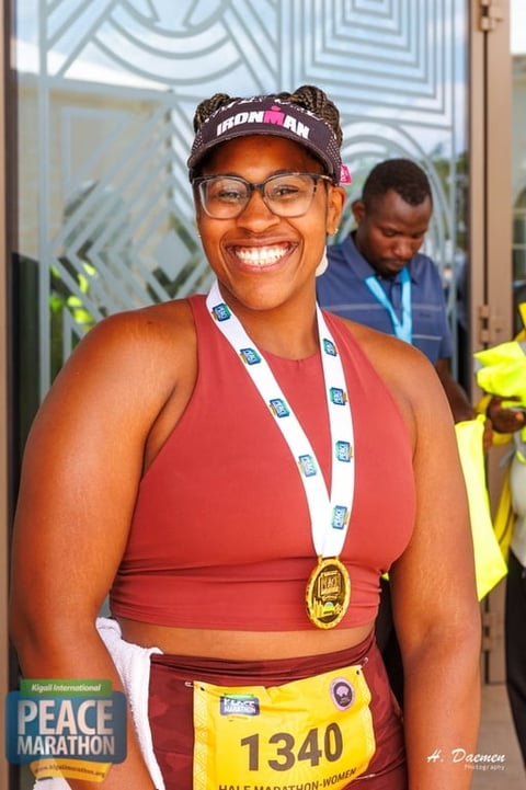 Woman wearing glasses and Ironman cap with medal at Peace Marathon finish line, smiling at camera