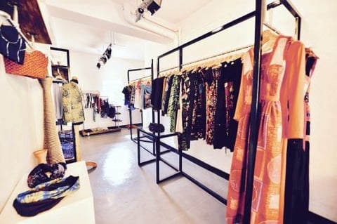Modern boutique clothing store interior with black metal racks displaying colorful dresses, textiles, and accessories on white walls and flooring