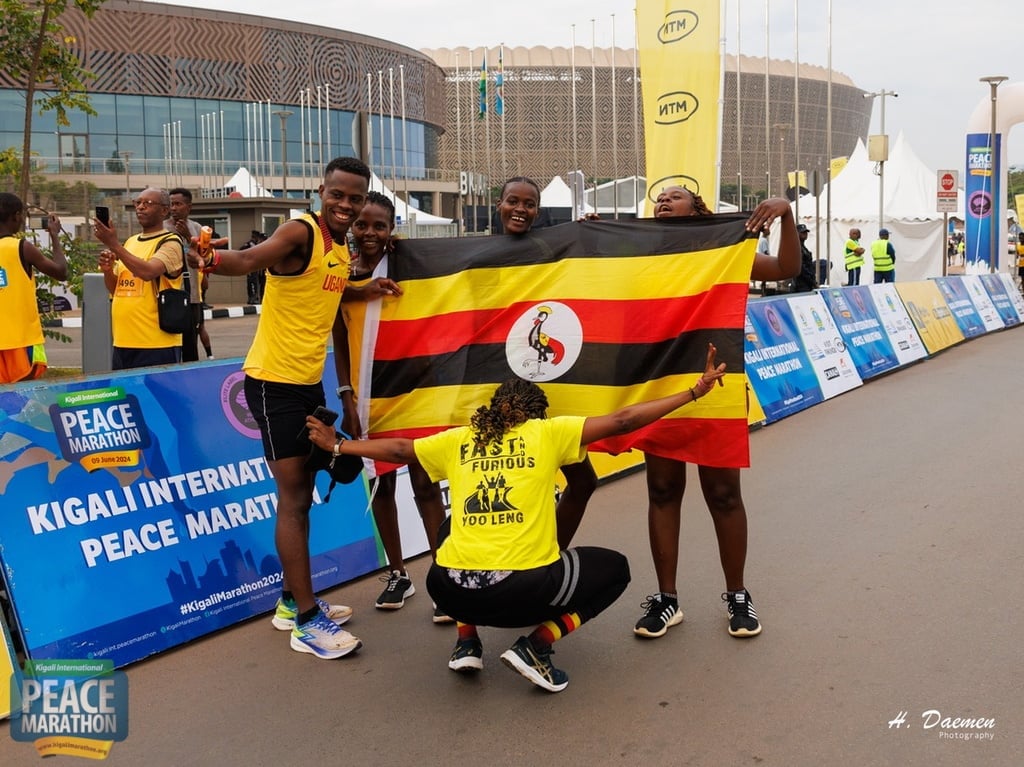 Runners holding Uganda flag at Kigali International Peace Marathon event with signage and urban background