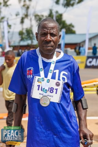 Runner wearing blue shirt and race bib 16 with medal at Peace Marathon event