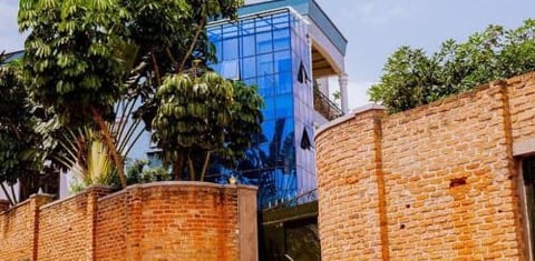 Modern blue building with large windows rising above red brick walls and green trees