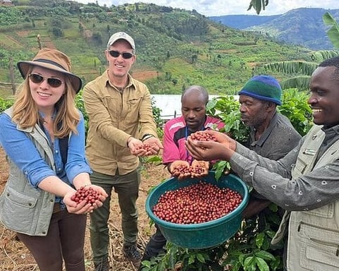 Group of five people holding coffee beans over a harvest basket in a green hillside farm