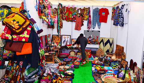 Vibrant textile and craft market display with colorful fabrics hanging on walls and merchandise arranged on tables and floor.