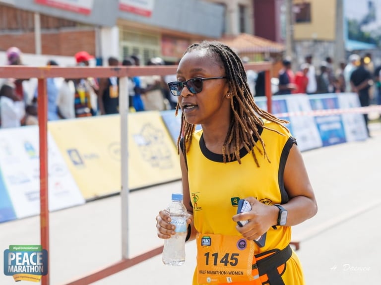 Woman in yellow marathon bib running with water, spectators and barriers visible in background