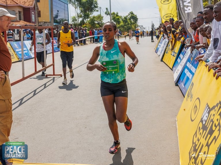Female runner in green bib during a marathon race, surrounded by spectators and yellow banner markers
