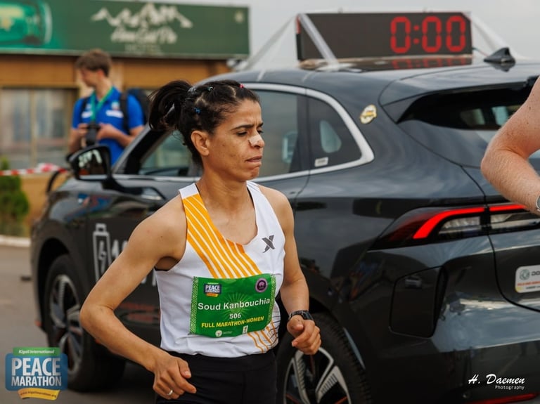 Female marathon runner wearing yellow and white bib passes a black car with digital timer during race