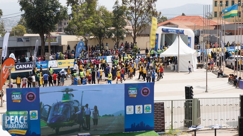 Outdoor peace marathon event with large crowds gathering in urban plaza near blue promotional banners and white tent structure